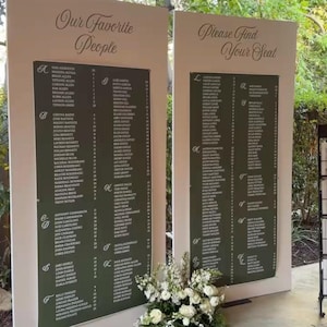 May include: Two tall, light-colored rectangular boards featuring dark green panels with white text. The left board is titled "Our Favorite People" and the right board is titled "Please Find Your Seat," both listing names and numbers with floral decor.