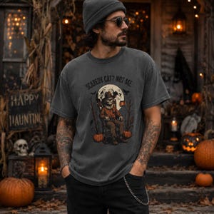 May include: A charcoal gray short-sleeve t-shirt featuring a graphic print of a scarecrow sitting in a chair under a full moon. The text above the illustration reads "SCAREDY CAT? NOT ME". The design includes orange pumpkins, bare trees, and flying bats.