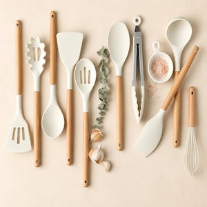 May include: A set of kitchen utensils featuring white silicone heads and light wood handles, including a slotted turner, pasta server, ladle, spatula, slotted spoon, solid spoon, metal tongs, a small bowl with pink salt, and a wire whisk.