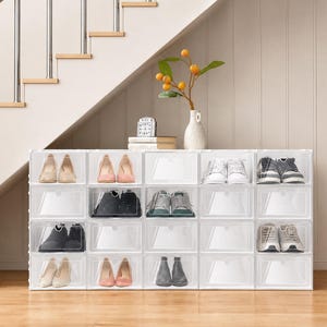 May include: A modular shoe storage unit consisting of twenty clear plastic stackable boxes arranged in four columns and five rows. Each box features a front-opening door, with various pairs of footwear stored inside several of the individual compartments.