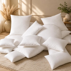 Peut inclure: Une collection de coussins blancs de différentes formes et tailles, incluant des modèles carrés, rectangulaires et ronds. Ces coussins blancs unis sont empilés, mettant en valeur leur rembourrage moelleux et leurs housses en tissu.