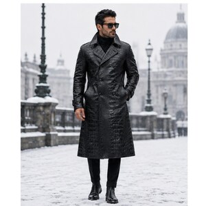 Può includere: Un trench nero con una trama testurizzata in pelle di coccodrillo, colletto ampio, chiusura a doppio petto e maniche lunghe. Il cappotto è indossato sopra un maglione a collo alto nero, pantaloni neri e stivali in pelle nera.
