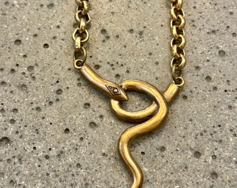 May include: A gold snake chain necklace with a gold snake pendant. The snake is curled up and has a small diamond-shaped detail on its head.