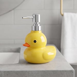 May include: A yellow ceramic soap dispenser shaped like a rubber duck with a bright orange beak, a black eye, and a metallic silver pump mechanism on top. The dispenser has a smooth, glossy finish and a rounded body, designed for liquid soap.