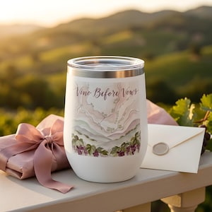 May include: A white stainless steel tumbler with a clear lid featuring a watercolour illustration of a vineyard landscape and the text "Vino Before Vows" in dark script. The design includes clusters of purple grapes and green leaves at the base.