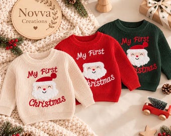 May include: Three long-sleeve knit sweaters in cream, red, and dark green. Each sweater features a white embroidered Santa Claus face and the red text "My First Christmas" on the front. The sweaters have a ribbed crew neckline and cuffs.