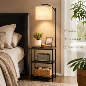 May include: A three-tier black metal side table with a built-in arched floor lamp featuring a beige fabric drum shade. The table holds a small potted plant, a candle, a picture frame, a speaker, and a woven basket on the bottom shelf.