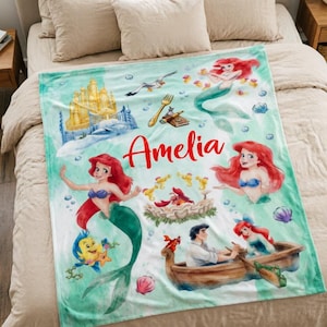 May include: A soft fleece blanket featuring a light green watercolor background with illustrations of Ariel, Flounder, Sebastian, and Prince Eric. The design includes a golden castle, a fork, a boat, and the name Amelia printed in red script.