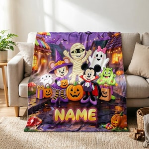 May include: A purple fleece blanket featuring a Halloween scene with cartoon characters dressed in costumes, including a witch, a mummy, a ghost, a vampire, and a green monster, with pumpkins, bats, and the word NAME printed in yellow letters.