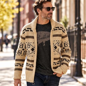 May include: A beige knit zip-up cardigan featuring a shawl collar and dark brown geometric patterns on the sleeves and chest, worn over a dark gray t-shirt with the word Pendleton printed in a script font across the front.