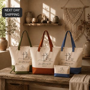 May include: Three canvas tote bags and three matching pouches in olive green, terracotta, and navy blue. Each item features a black line drawing of a cross, a leafy branch, a heart, and the text He restores my soul Psalm 23:3 on a cream background.