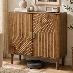 May include: A wooden cabinet with two doors featuring a white arched line pattern, gold vertical handles, and four tapered legs. The cabinet surface holds two stacked books, a white vase with greenery, and a small rectangular radio.