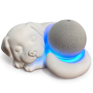 May include: A white matte sculpture of a sleeping puppy with a circular cutout designed to hold a spherical smart speaker. The base of the cutout features a bright blue LED light ring that illuminates the bottom of the gray fabric-covered speaker.