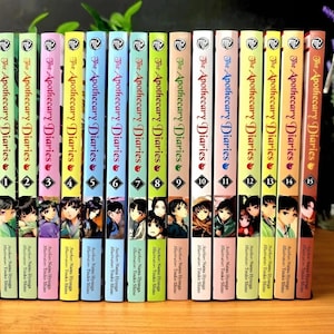 Può includere: Una collezione di quindici volumi manga intitolati The Apothecary Diaries, disposti fianco a fianco. Ogni dorso presenta un colore pastello unico, il titolo della serie, un numero di volume da 1 a 15 e una piccola illustrazione di un personaggio.