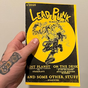 May include: A Lead Punk magazine issue 1/2026 with a yellow and black cover. The graphic features a stylized character holding a knife and a weapon, set against a large yellow circle. Text includes Lost Planet, On The Desk, and And Some Other Stuff.