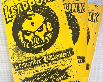 Op de afbeelding: Een geel zine getiteld LEADPUNK 2/2026 met zwarte inktillustraties en tekst. De omslag bevat een gestileerde figuur met helm, vleermuizen en de tekst I REMEMBER HALLOWEEN, ALL THE SAME BULLSHIT YOU'VE COME TO EXPECT.. NOW IN DELICIOUS PUMPKIN SPICE FLAVOR! BLOODBOWL! NECROMUNDA! CORN! ..WHATEVER.