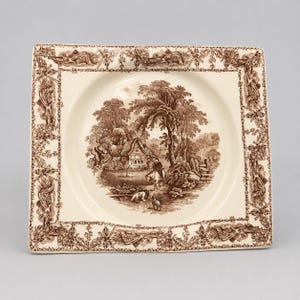 May include: A square ceramic plate with a cream-colored base and a brown transferware print. The center features a rural landscape with a cottage, a person on horseback, and trees. The border displays a detailed floral and ribbon pattern.