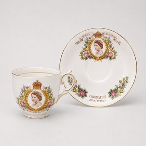 Op de afbeelding: Een witte porseleinen theekop en schotel set met een portret van koningin Elizabeth II, een gouden kroon en bloemmotieven. De tekst luidt Queen Elizabeth II en Coronation June 2nd 1953. De set is afgewerkt met een gouden rand op de randen en het oor.