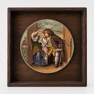 Pode incluir: Um prato decorativo circular de cerâmica com uma ilustração colorida de duas figuras em trajes históricos, intitulado UNCLE TOBY na parte inferior, inserido numa moldura quadrada de madeira castanho-escura com acabamento liso e bordo dourado.