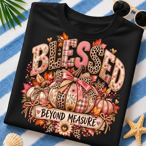 May include: A black t-shirt featuring the word BLESSED in large, patterned letters with leopard print, plaid, and floral designs. Below, three pumpkins are decorated with bows, surrounded by autumn leaves and the text BEYOND MEASURE.