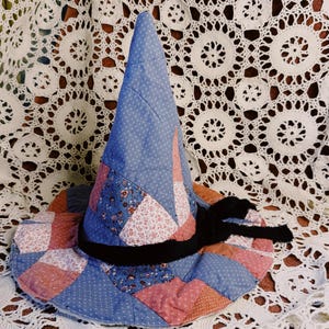 May include: A conical hat constructed from a patchwork of quilted fabric pieces in shades of blue, pink, and white with floral and dotted patterns. A black velvet ribbon is tied around the base of the crown, contrasting with the colorful textile.