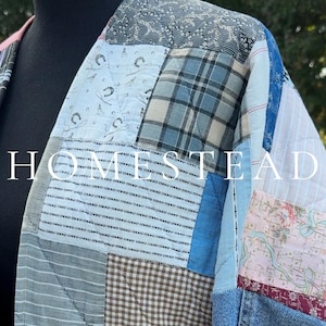 May include: A quilted jacket featuring a patchwork design of various fabrics including blue denim, plaid, striped, and floral patterns. The garment displays the word HOMESTEAD in white capital letters across the front, with visible stitching throughout.
