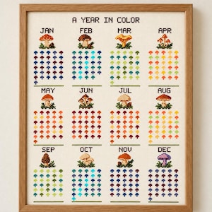 Op de afbeelding: Een ingelijste kruissteekkalender getiteld A YEAR IN COLOR, met twaalf maandelijkse secties. Elke maand toont een unieke paddenstoelillustratie boven een raster van kleine, gekleurde paddenstoelpictogrammen voor de dagen.