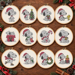 May include: Twelve circular wooden embroidery hoops containing cross-stitch patterns of Snoopy and Woodstock in various Christmas scenes, including wearing Santa hats, decorating a tree, holding gifts, candy canes, and ice skating on white fabric.