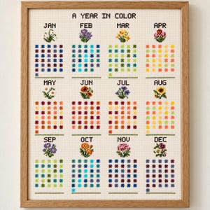 May include: A framed cross-stitch embroidery titled A YEAR IN COLOR, featuring twelve monthly sections. Each month displays a small floral motif above a grid of colored flower icons representing daily color tracking for the entire year.