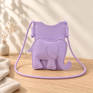 Può includere: Una borsa a tracolla color viola chiaro di forma rettangolare verticale con bordo superiore sagomato e un'evidente applicazione a forma di elefante sul davanti. La borsa include una sottile tracolla in corda viola abbinata sui lati.