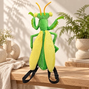 May include: A plush praying mantis backpack featuring a bright green body with yellow wings, two orange antennae, and large eyes. The back of the insect has a central zipper closure, and the bag includes adjustable black straps for carrying.