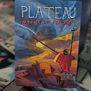 May include: A rectangular game card titled PLATEAU MOUNTAIN PLAINS featuring a painted landscape with a figure in a red cloak holding a long spear and a banner. The scene depicts a sunset over rocky cliffs with a dark, swirling sky above.