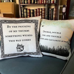 May include: Two square throw pillows featuring literary quotes. The left pillow is off-white with a black ornate border, a skull wearing a crown, and the text: By the pricking of my thumbs, something wicked this way comes. The right pillow features the text: Double, double toil and trouble, fire burn and cauldron bubble, with a black silhouette of a forest and birds.