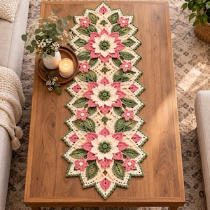Può includere: Un lungo runner da tavola rettangolare all'uncinetto con un motivo floreale ripetuto. Il design presenta grandi fiori stratificati rosa e crema con centri verde scuro, circondati da intricati motivi a foglia verde e una trama a rete crema.