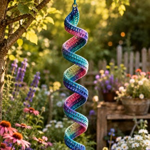 May include: A hanging spiral decoration made of crocheted yarn featuring a gradient of colors including blue, purple, pink, and yellow. The structure is a long, twisted coil with an open-work stitch pattern, suspended from a small circular ring.