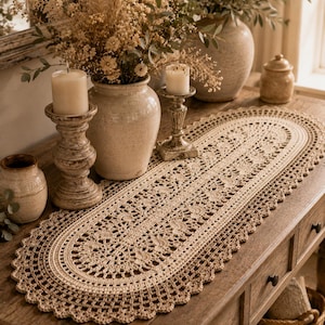 May include: An oval-shaped beige crochet table runner featuring an intricate openwork pattern with a scalloped edge. The runner is crafted from fine thread and displays a detailed, repeating geometric design throughout its entire length.