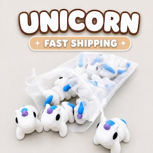 May include: A collection of small white unicorn figurines with blue manes and tails and purple horns, contained within a sheer white drawstring organza bag. The text UNICORN is displayed in large white letters with a brown outline above the bag.
