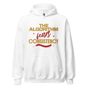 May include: A white hooded sweatshirt featuring the text THE ALGORITHM in gold, the word fears in a red script font, and the word CONSISTENCY in gold. The design includes small red star accents and a red horizontal brush stroke underneath.