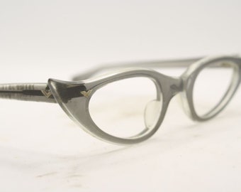 May include: Gray cat-eye glasses with gold accents. The glasses have a thin metal frame and clear lenses.