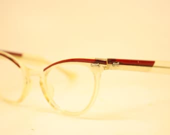 May include: Clear cat-eye spectacles with a red accent on the top frame and temples. The glasses have a retro style, with a light-coloured frame and clear lenses. The design is simple and elegant.