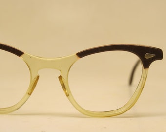 May include: A pair of vintage eyeglasses with a brown and clear plastic frame. The frame has a cat-eye shape and a small metal detail on the side.