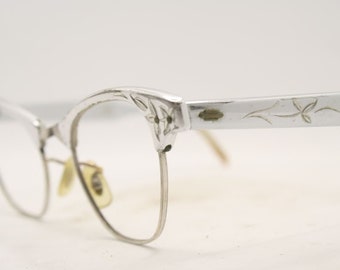May include: Silver cat-eye glasses with a floral design on the arms.