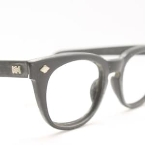 Op de afbeelding: Zwarte plastic gemonteerde bril met een kattenoogvorm. De bril heeft een zilveren logo aan de zijkant.