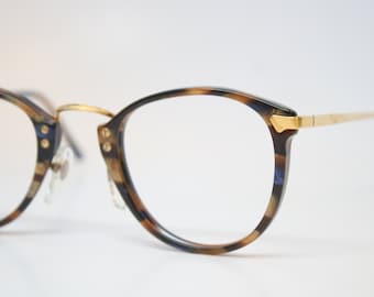 May include: Round eyeglasses with a tortoiseshell pattern on the frames. The glasses have gold-colored metal accents on the bridge and temples. The lenses are clear, and the overall design is classic and stylish.