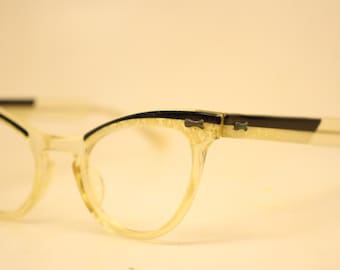 May include: Vintage cat-eye spectacles with a light yellow frame and black detailing. The glasses have a classic shape with a slightly pointed upper edge. The temples are a mix of light yellow and black.
