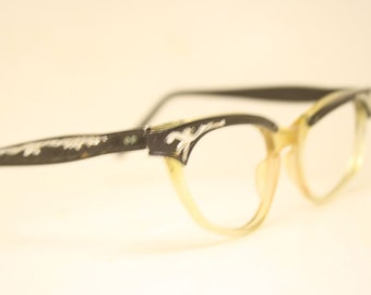 May include: Black cat-eye glasses with a silver design on the frames and clear lenses.