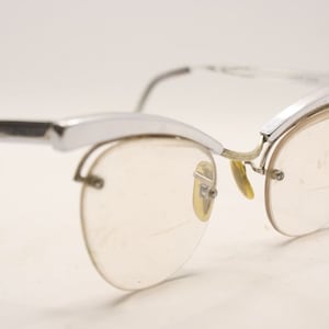 Könnte beinhalten: Silberfarbene Cat-Eye-Brille mit klaren Gläsern. Die Brille hat einen dünnen Metallrahmen und ein filigranes Design.