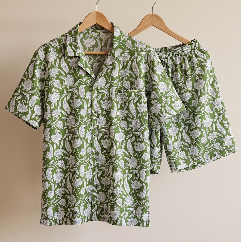 May include: A short-sleeve button-down shirt and matching shorts set in a vibrant olive green color. The fabric features a repeating white floral and paisley pattern throughout. The shirt has a notched collar and a single chest pocket.