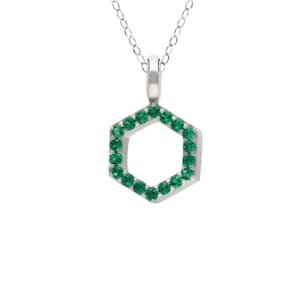 Può includere: Una collana in argento con un ciondolo esagonale. Il ciondolo è incastonato con piccole pietre preziose rotonde di un verde vibrante lungo tutto il perimetro, sospeso a una sottile catenina d'argento fissata alla sommità dell'esagono.