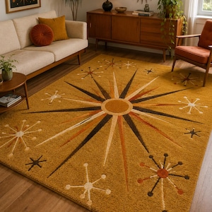 May include: A rectangular area rug in a mustard yellow hue featuring a large central starburst pattern with radiating rays in shades of brown, orange, and cream. The design includes smaller scattered starburst motifs across the surface.